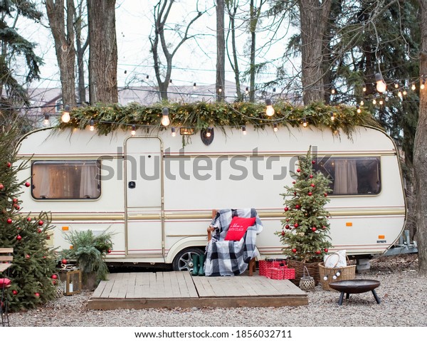 Vintage old travel trailer with Christmas\
decorations, Christmas tree, chair and Christmas lights. Cozy home,\
camping before Christmas\
holidays.