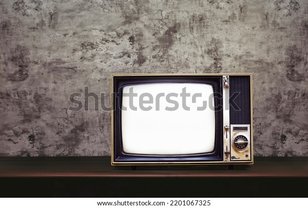 Vintage old TV on wooden table with\
concrete wall background with copy space on the\
left.