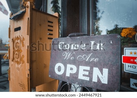 Vintage open sign on sidewalk outside business. Cursive  Come In , bold  OPEN . Rustic charm, wooden structure, inviting interior. Ideal for small business, boutique, cafe.