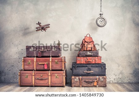 Vintage outdated trunks luggage, old antique valises, classic leather backpack, flying wooden toy plane and hanging big clock front concrete background. Travel by air concept. Retro style photo