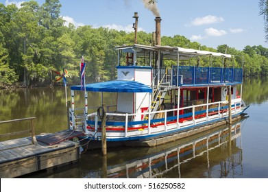Vintage paddlwheel steamboat painted in old-fashioned American red, white, and blue reflects on the waters of a swamp in the deep American South