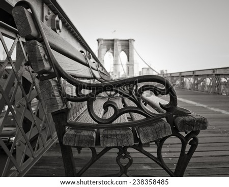 A vintage park bench on the Brooklyn Bridge facing Manhattan in black and white.