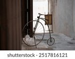 A vintage penny-farthing bicycle leans against a wooden door in a narrow, dimly lit alley. The scene evokes nostalgia and historical charm, contrasting the old-world bicycle with the rustic place.