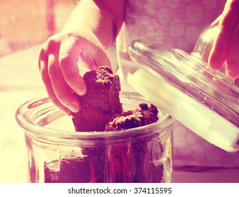 Vintage Photo Of A Child's Hand Reaching For A Piece Of Chocolate Brownie From A Glass Cookie Jar. Toned Image. Soft Focus. Vignette