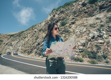 Vintage Photo Female Hiker Pick Up Local Paper Map Looking Choosing Travel Destination At Road Trip On Highway 1 California Usa. Confident Girl Backpacker In Sunglasses Walking On Sunny Day Outdoor