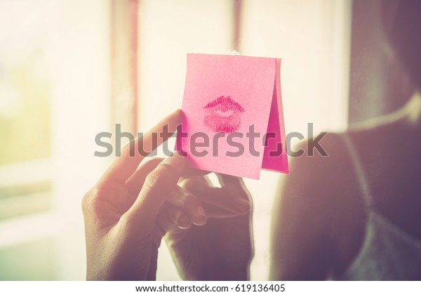 鏡にキスの口紅の跡がついた紙のメッセージを手に持つ手のビンテージ写真 朝の光の中で セクシーな女の子の赤い唇がノートにキスする 夫婦からのロマンチックなメッセージ の写真素材 今すぐ編集
