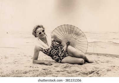 Vintage photo of woman resting on beach in swimsuit with umbrella (early 1960's)
