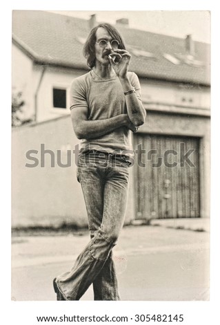 Vintage photo from young fashion smoking man wearing typical 1970s clothing. Retro picture with original film grain and scratches.