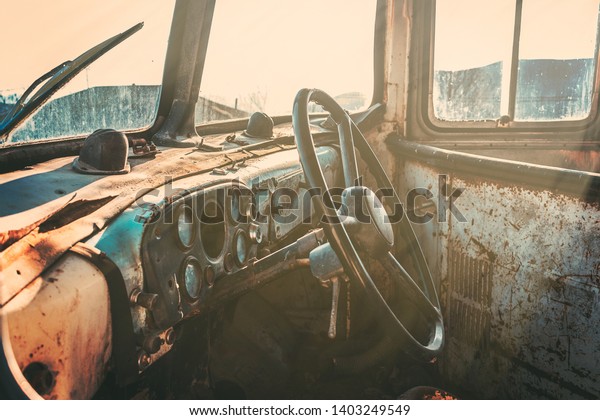 Vintage photography of used and rusty\
abandoned school bus with cluster of gauges and steering wheel in\
focus while warm sunshine coming through the\
windows