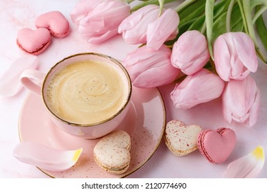 Vintage pink coffee cup, tulip flowers and french sweet cookies macarons macaroons  on marble background.  Heart shape macarons, cup and bouquet of tulip. Pastry shop love or birthday card with copy 