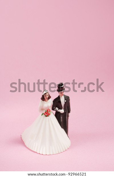 Vintage plastic wedding cake decoration on\
pink background.