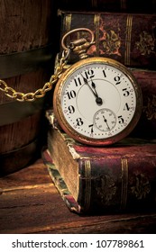 Vintage pocket clock showing a few minutes to midnight over ancient books in Low-key. Concept of time,the past or deadline.