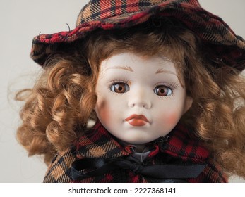 Vintage porcelain doll girl with brown eyes with red flowing curly hair in a checkered black and red dress and hat