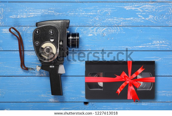 Vintage portable movie film\
camera Videotape VHS gift tied red bow on a blue wooden\
background.