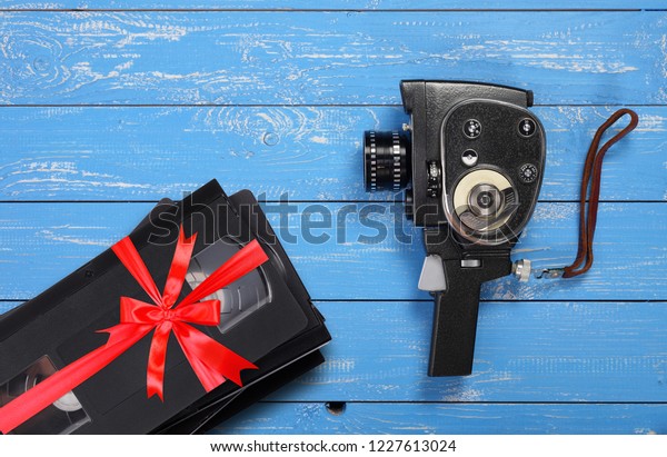 Vintage portable movie film\
camera Videotapes VHS gift tied red bow on a blue wooden\
background.