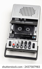 VIntage portable tape recorder with open cover and compact cassette inside compartment. The device features built-in speaker microphone and simple control buttons at the bottom