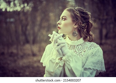 Vintage Portrait Of A Beautiful Noble Lady In A White Dress Standing In The Old Park. Hair And Makeup, Late 19th Century. Historical Reconstruction Of The Victorian Era. 