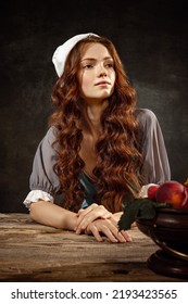 Vintage portrait of young adorable redhead girl in image of medieval person, peasant woman in renaissance style dress isolated on dark background. Comparison of eras, beauty, history, art
