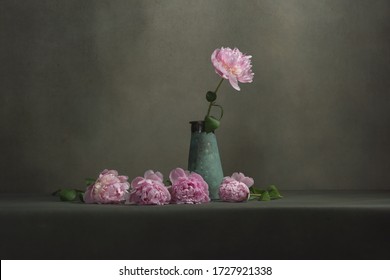 Vintage pottery vase with one peony and some peonies lying next to it on a table in a grey room.