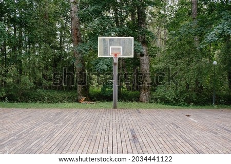 Vintage Recreational basketball hoop in orange colour in park. Plank floor, metal support and plastic screen in front of green forest. Ideal place for street ball. Iconic central composition.
