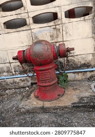 Vintage red fire hydrant with rusty chains against weathered concrete wall.