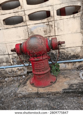 Vintage red fire hydrant with rusty chains against weathered concrete wall.