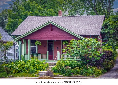 Vintage Red Wood Shingled House With Green Trim And Porch Swing And Landscaping Including Hydrangeas.