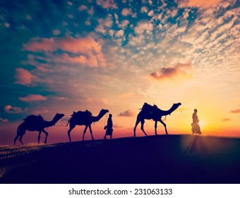 Vintage retro effect filtered hipster style image of  Rajasthan travel background - two indian cameleers with camels silhouettes in Thar desert dunes on sunset. Jaisalmer, Rajasthan, India