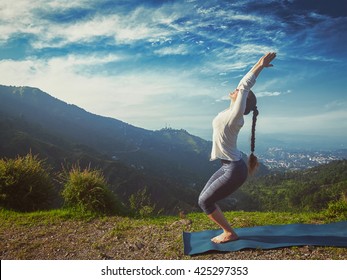Vintage retro effect hipster style image of young sporty fit woman doing yoga asana Utkatasana (chair pose) outdoors in mountains Himalayas in the morning. Himachal Pradesh, India