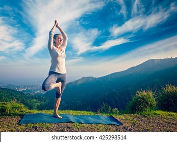 Vintage retro effect hipster style image of woman practices balance yoga asana Vrikshasana tree pose in Himalayas mountains outdoors in the morning. Himachal Pradesh, India. Panorama