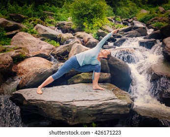 Vintage retro effect hipster style image of fit woman practices yoga asana Utthita Parsvakonasana -  extended side angle pose outdoors at water