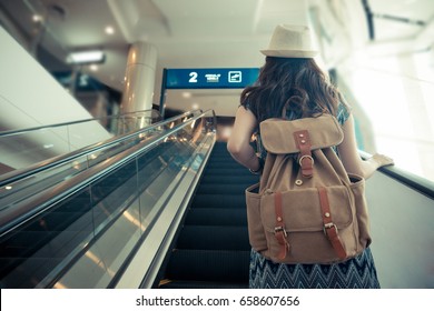 vintage retro film color photo. back view of female traveler carrying backpack and standing on electric escalator going to gate when she arrived airport.