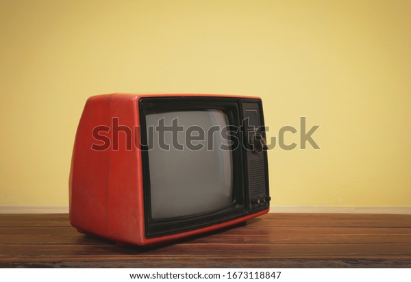 Vintage, Retro red old tv on wooden table\
with yellow concrete wall\
background.
