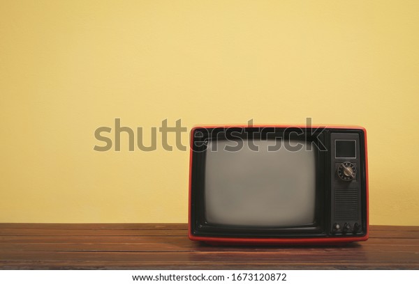 Vintage, Retro red old tv on wooden table\
with yellow concrete wall\
background.