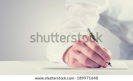 Vintage retro style image of a man signing a document or writing notes on a sheet of paper, close up of his hand with copyspace to the left.