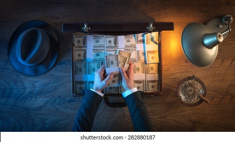 Vintage rich businessman's desk with a briefcase filled with dollar packs, he is counting paper currency