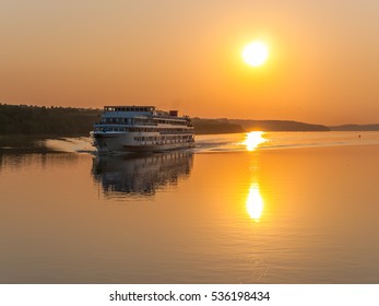 vintage river boat on the background of orange sunset and silhouette shoreline reflecting glows in water surface, Volga, Russia