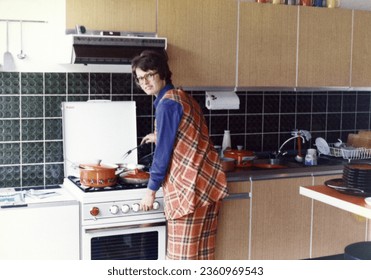 Vintage roll fillm, 1970's woman wearing an orange squared pant and vest cooking dinner on a gas stove. - Powered by Shutterstock