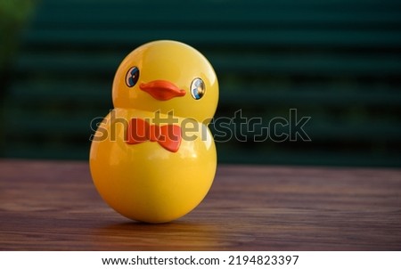Vintage roly-poly toy shaped like a cute yellow chick. Tumbler toy isolated on an outdoor wooden table at sunset.