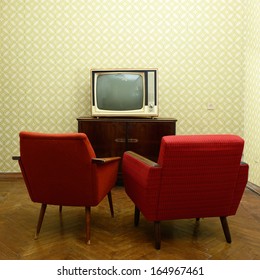 Vintage room with two old fashioned armchairs and retro tv over obsolete wallpaper
