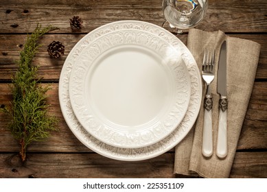 Vintage Or Rustic Christmas Table Setting From Above. Elegant Empty White Plate, Cutlery On Linen Napkin And Natural Pine Tree Branch On Rustic Planked Wood - Country Style.