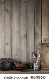 Vintage rustic kitchen still life: silver glass holder with cutlery, ceramic dishware, cast iron cauldron and cutting boards against vintage wooden background.