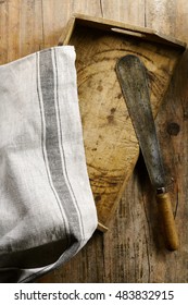 Vintage Rustic Kitchen Utensils And Cloth With A Large Pizza Knife On An Old Wooden Tray Style Cutting Board Viewed Close Up From Above