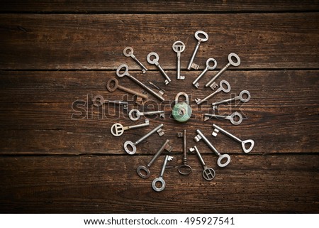 Vintage rusty padlock surrounded by old keys on a weathered wooden background

