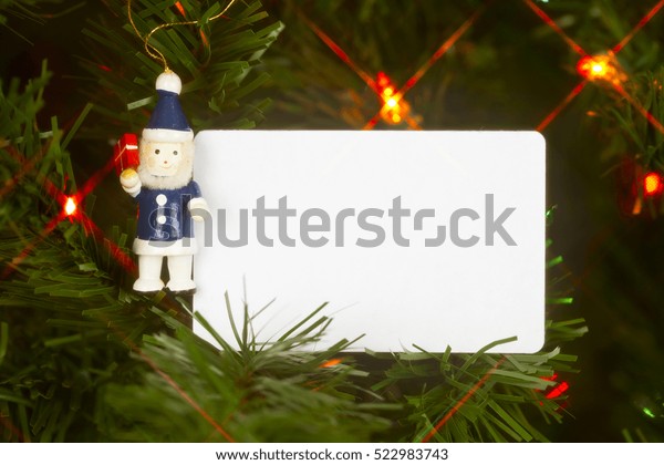 Vintage santa in a blue suit\
hanging on a traditional christmas tree with white car for copy\
space
