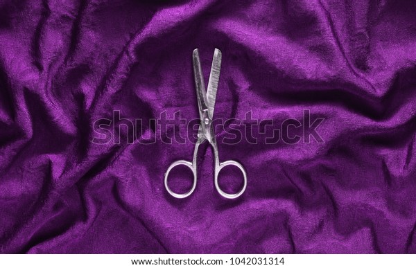 Vintage\
scissors on a violet fabric background. Top\
view.