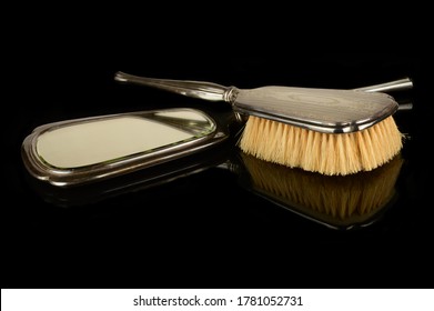 A Vintage Set Of A Handheld Sterling Silver Mirror And Hair Brush Isolated Over A Black Reflective Surface.