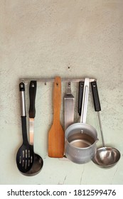 vintage set of kitchen fixtures hangs on an empty wall. A wooden spatula weighs between the metal tools   - Shutterstock ID 1812599476