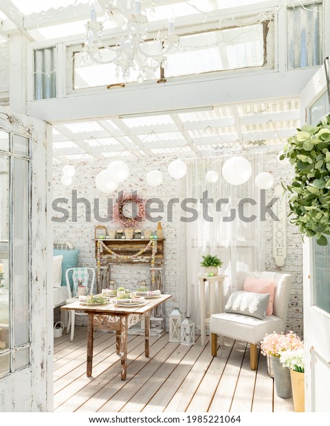 Vintage\
shabby chic garden room. A white distressed brick wall and antique\
farm table with diy faux fireplace, chandelier, paper lanterns and\
linen chair create a playful whimsical\
space.