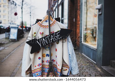 Vintage sign with a background of different vintage clothing on a street. White vintage sweater with embroidered flowers.  